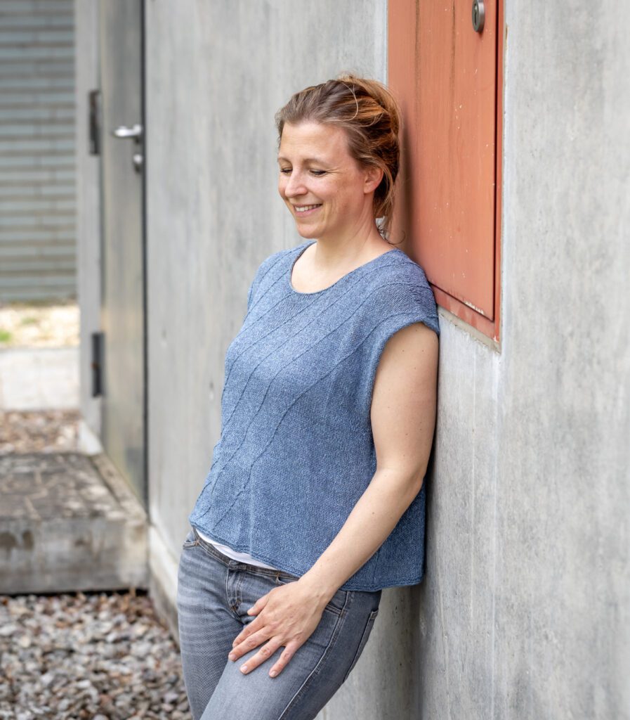 Marisa is wearing the short-sleeved shirt "Big in Japan" by Katrin Schneider. She is leaning against a wall.